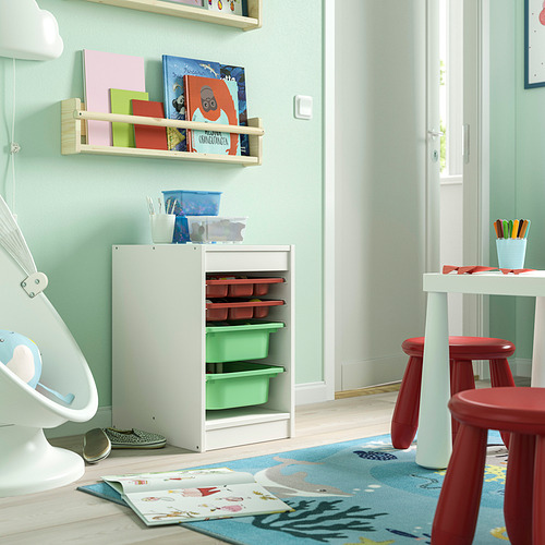 Sala de juegos para niños con unidad de almacenamiento blanca TROFAST, taburetes rojos, libros y alfombra de colores.