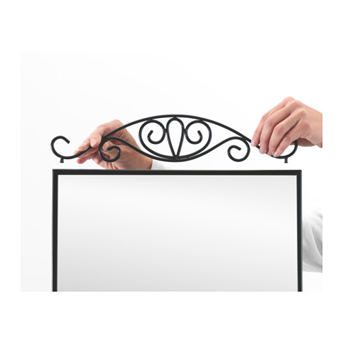 Dos manos unen un arco metálico decorativo a un marco rectangular, probablemente la parte superior de un espejo, lo que mejora su estilo y utilidad para colgar artículos.