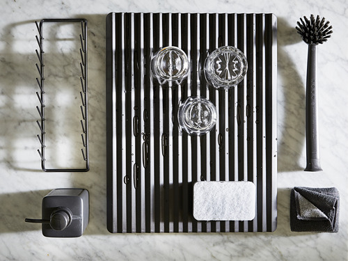 Accesorios de cocina negros que incluyen tendedero, cepillo, soporte para esponjas y estropajo sobre superficie de mármol.