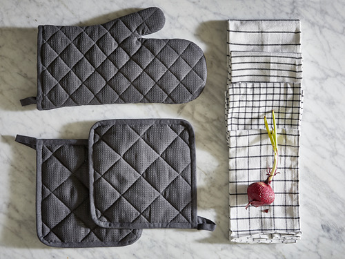 Una superficie de mármol muestra guantes de cocina y agarraderas acolchados de color gris oscuro, además de toallas a rayas con remolacha roja y puerros.
