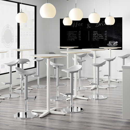 Cafetería moderna con mesas altas y taburetes blancos. El menú de Blackboard dice café y bebidas. Suelo de madera clara, lámparas colgantes blancas en el techo.