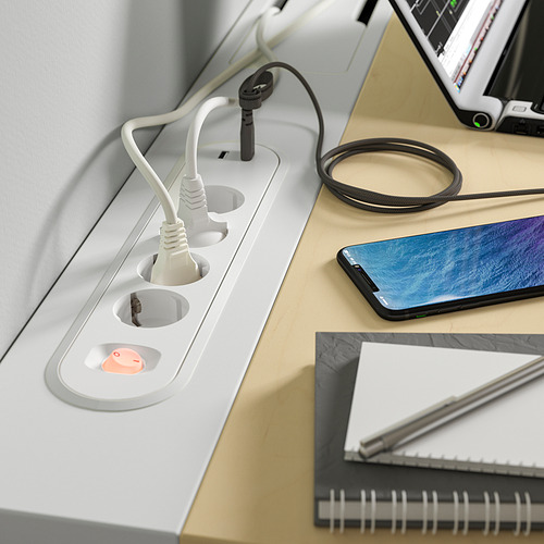 Escritorio blanco con regletas y cables incorporados; teléfono inteligente, computadora portátil y bolígrafo en la parte superior.