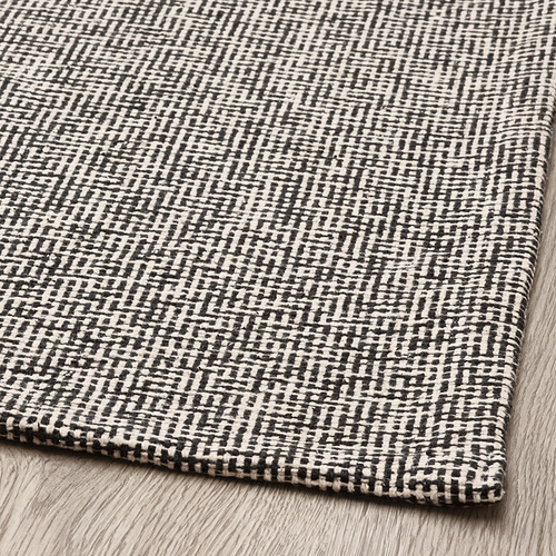 Alfombra estampada en blanco y negro, tejido texturizado, colocada sobre suelo de madera.