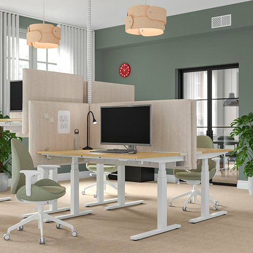 Moderna oficina con mamparas de escritorio MITTZON, sillas verdes y luz natural a través de grandes ventanales. El reloj rojo agrega color y distracciones mínimas para concentrarse.
