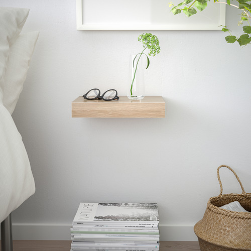 Habitación minimalista con estantería para vasos, jarrón y revistas. También se ve la cesta tejida y la cama.