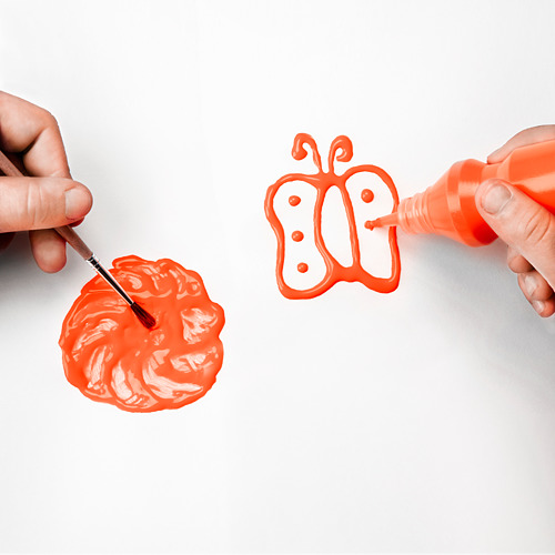 Manos de niños pintando mariposa con pincel naranja y exprimiendo pintura de la botella sobre superficie blanca.