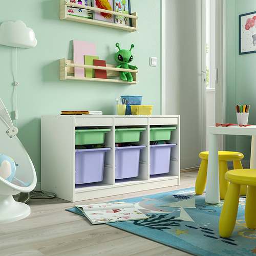 Unidad de almacenamiento TROFAST en blanco con cajas de colores en la habitación de los niños, rodeada de taburetes amarillos y una alfombra.