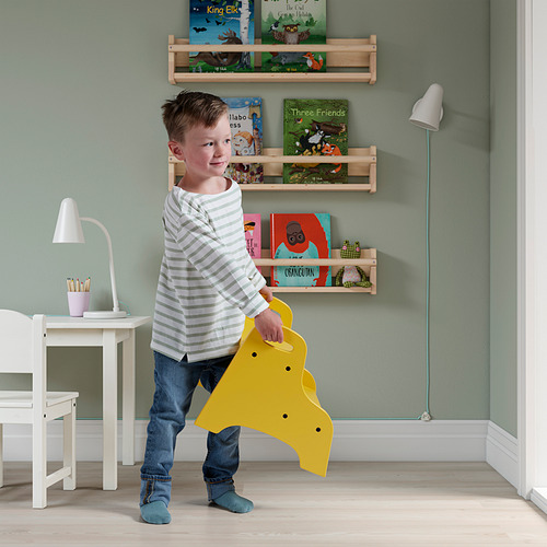Descripción de la imagen: un niño sosteniendo un taburete amarillo en una habitación con estanterías y un escritorio.