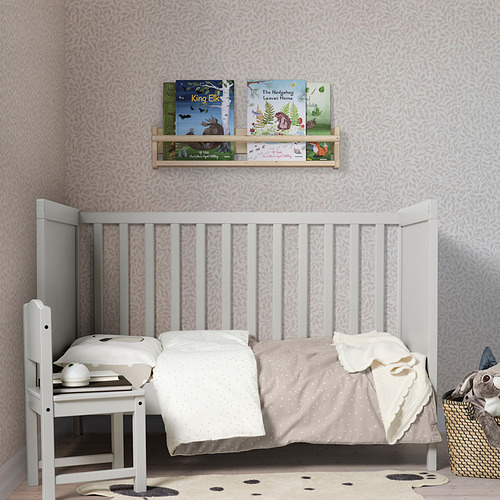 Habitación infantil con alfombra DRÖMSLOTT, cuna blanca, estantería de pared con libros. La alfombra gris suave cabe debajo de la cuna.
