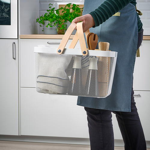 Persona que sostiene una cesta de alambre con asas de madera, que contiene utensilios de cocina, en una cocina. El diseño de malla de las cestas permite que el contenido sea visible.
