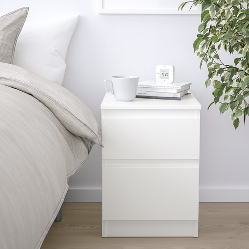 Mesita de noche KULLEN, blanca con taza, libros, reloj, planta verde.