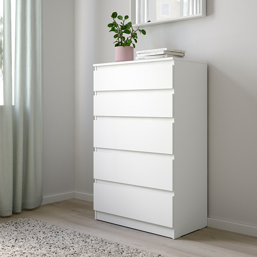 Cómoda KULLEN blanca en esquina dormitorio, con libros y plantas, cajones altos y anchos.