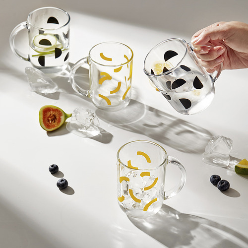 Con la mano sosteniendo una taza de vidrio transparente, otras tres cerca, cada una con giros cítricos y hielo. Uno tiene arándanos. La mesa tiene frutas en rodajas.