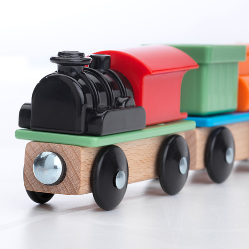 Tren de juguete brillante con motor negro y vagones coloridos, sobre rieles de madera clara.