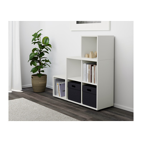 Estantería modular blanca EKET, con cajas abiertas y de almacenamiento. Tiene capacidad para libros y contenedores suministrados. Fijado a la pared para mayor estabilidad.