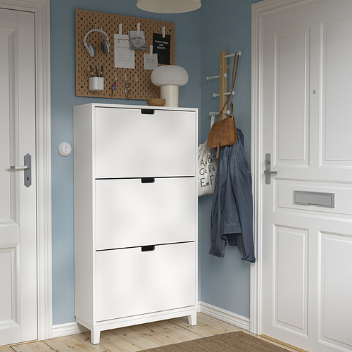 Zapatero STÄLL blanco moderno entre puertas, pared azul, suelo de madera, tablero perforado con accesorios.