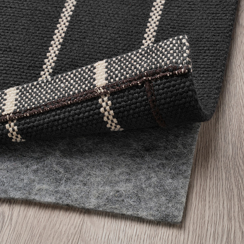 Una alfombra de algodón gris doblada con rayas blancas, perfecta para pasillos, mostrada sobre un suelo de madera.