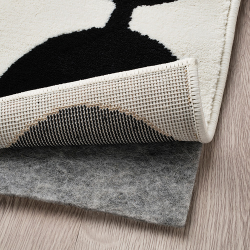 Alfombra estampada en blanco y negro con fieltro antideslizante debajo, colocada sobre suelo de madera.