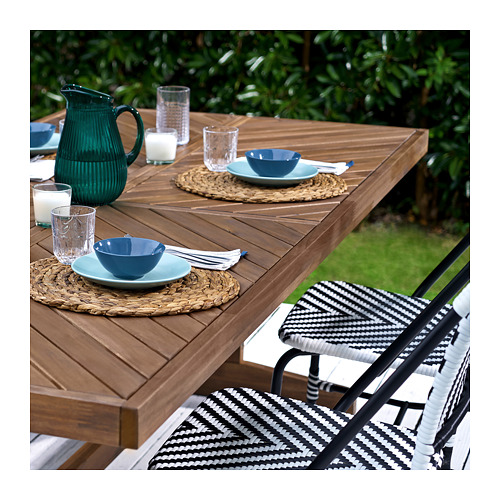 Patio al aire libre con mesa de madera, sillas blancas y negras, cuencos azules, vasos y jarra verde.