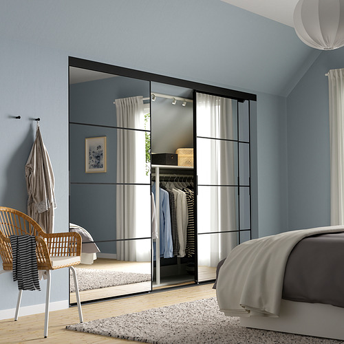 Dormitorio moderno de color azul cielo con puertas de armario con espejo SKYTTA que realzan la amplitud, marcos negros, ropa de cama blanca, silla de mimbre y decoración neutra.
