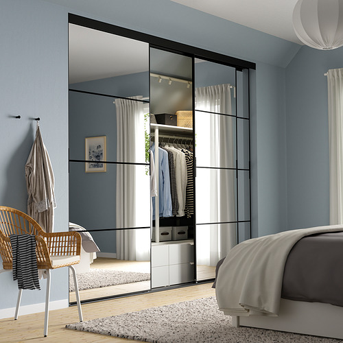 Dormitorio con gran puerta de armario azul claro con paneles de espejo. Cama gris, silla de mimbre y prenda colgada a la vista.