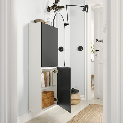 Moderno mueble de almacenaje BESTÅ de ikea blanco y negro con una puerta abierta, que exhibe libros y cajas.