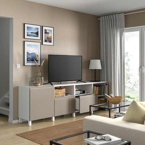 Banco de tv blanco BESTÅ en salón. Televisión, decoración, libros. Gran ventanal con cortinas. Sofá beige junto a mesita de madera.