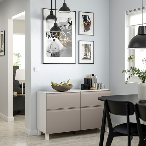 Comedor moderno con aparador BESTÅ gris claro, sillas negras y lámparas colgantes. Obra de arte y frutero en el aparador.