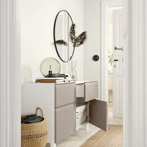 Moderno aparador blanco BESTÅ con puertas abiertas que dejan ver compartimentos de almacenamiento y estantes, rematados con elementos decorativos.