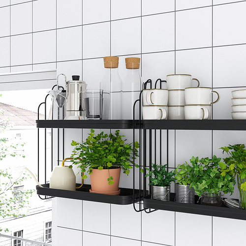 Los modernos estantes de pared de metal negro sostienen tazas blancas, frascos de vidrio y plantas verdes en una habitación con azulejos blancos, que combinan estilo con elementos naturales.