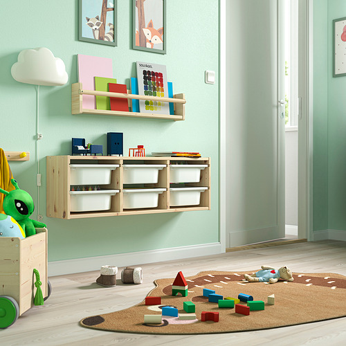 Sala de juegos con estantes de almacenamiento de madera clara TROFAST, juguetes coloridos, libros y una alfombra beige.