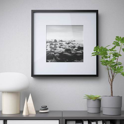 Unas rocas enmarcadas en blanco y negro se encuentran sobre un armario, rodeadas de una lámpara, plantas y piedras decorativas. El marco muestra la foto de forma destacada.