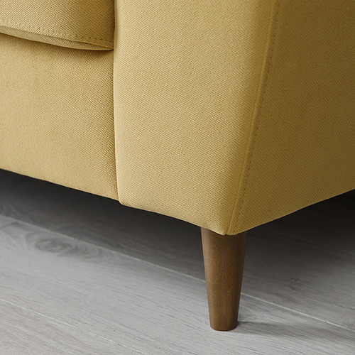 Primer plano del sofá amarillo, que muestra una pata de madera resistente y una tela afelpada, que enfatiza la comodidad y el diseño moderno.