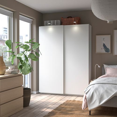 Dormitorio moderno con armario PAX blanco, suelo de madera, cama, planta y obras de arte.