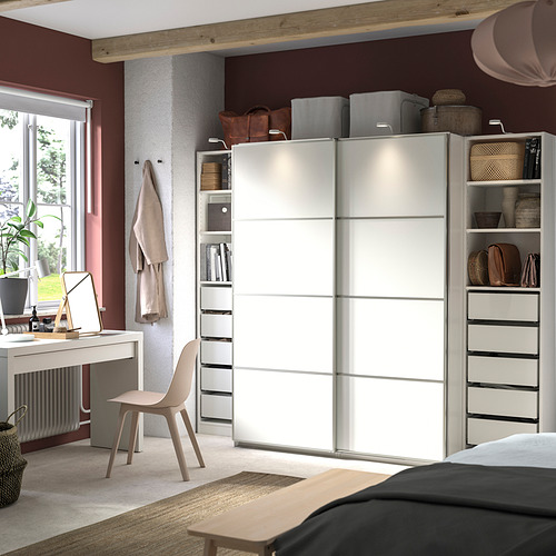 Dormitorio moderno con un gran armario blanco con puerta corredera, silla beige, escritorio y alfombra, con estantes y cajones organizados.