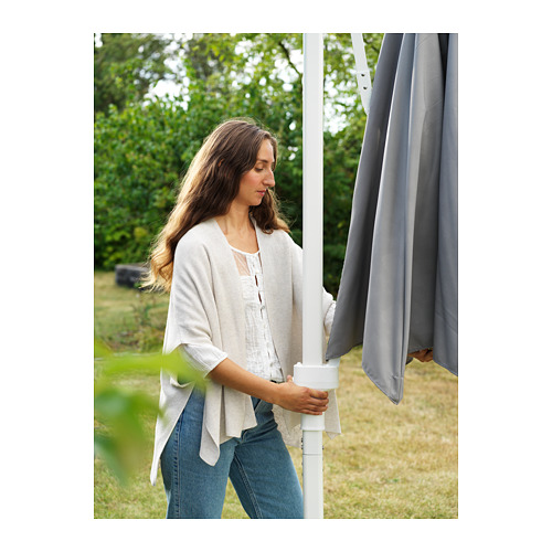 Una mujer ajustando una sombrilla de exterior HÖGÖN blanca con un dosel gris. La sombrilla está diseñada para reducir la presión del viento y bloquear el 96% de los rayos UV.