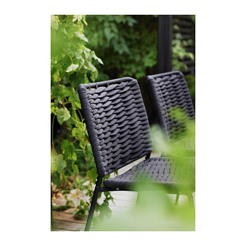 Sillas de exterior de mimbre negro, apiladas, con plantas verdes al fondo.