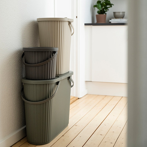 Tres contenedores apilables en beige y gris para la clasificación de residuos cerca de la pared.