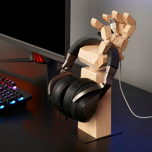 Una figura de madera sostiene auriculares, manteniéndolos organizados y al alcance de la mano en un escritorio.
