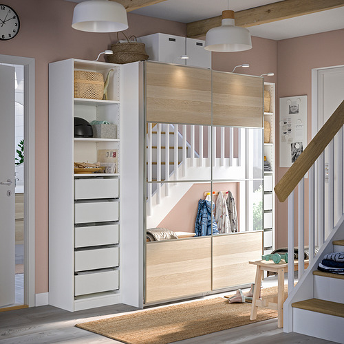 Una habitación con armario PAX blanco y de madera clara. Dispone de cajones y puertas correderas con iluminación incorporada. Hay una escalera a la derecha.