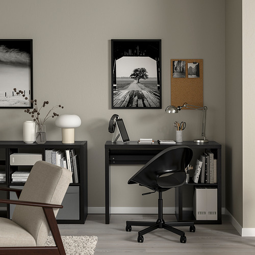 Configuración moderna de oficina en casa: escritorio negro con computadora portátil, lámpara y silla. Arte enmarcado en negro sobre paredes grises. Silla y lámpara beige en estantería.