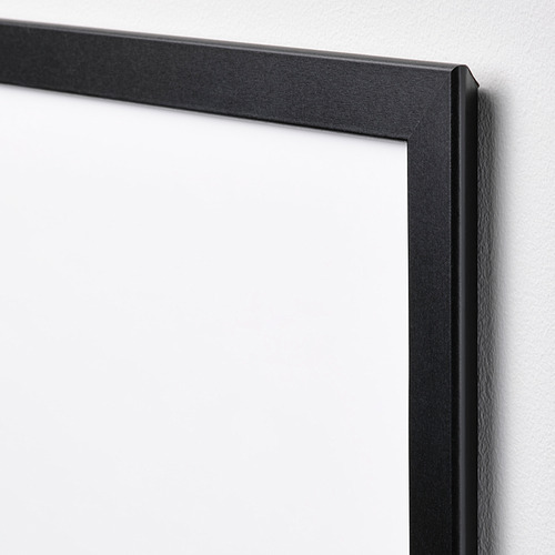 Marco de fotos negro con bordes lisos montado sobre una pared blanca. Acabado de alta calidad, líneas suaves visibles.