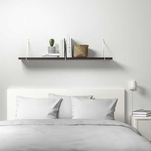 Moderno dormitorio blanco con estantería de pared BERGSHULT. El estante contiene libros, cesta y plantas. Cama de abajo con ropa de cama blanca, mesita de noche con libros.