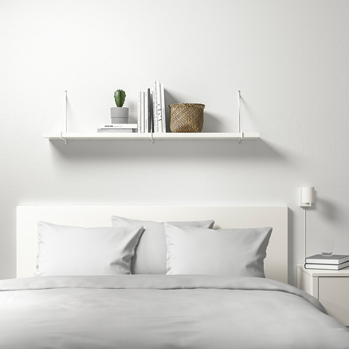 Dormitorio minimalista: la estantería blanca BERGSHULT contiene libros, plantas, cestas; Cama blanca con almohadas. El estante es grande en comparación con los artículos.