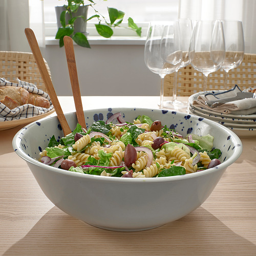 Las pinzas de madera para ensaladas descansan en un plato de ensalada de pasta, rodeadas de platos y copas de vino.