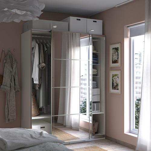 Dormitorio moderno con armario PAX, puertas correderas con espejos, tela gris, ropa organizada, cama blanca, gran ventanal.