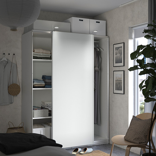 Un moderno dormitorio gris con un armario PAX con puerta corredera blanca con estantes y espacio para colgar, complementado con arte en la pared y una silla de madera.