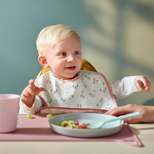 El bebé con un babero floral se sienta en una silla alta, comiendo.