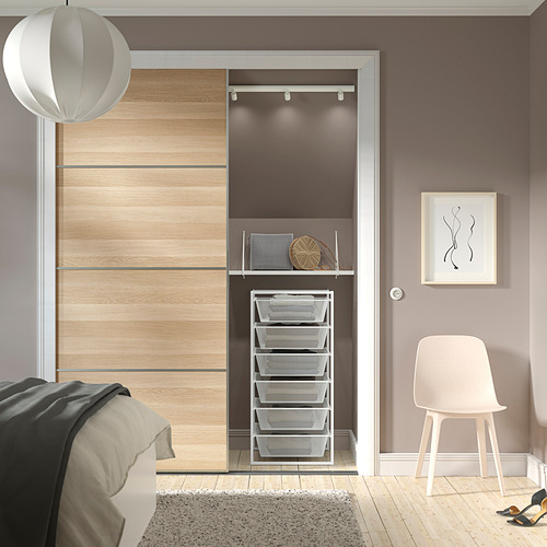 Armario JONAXEL de madera con cestas de malla, barra para colgar y estante superior. Una lámpara colgante blanca y una silla minimalista. Cuidadosamente organizado con cestas redondeadas.