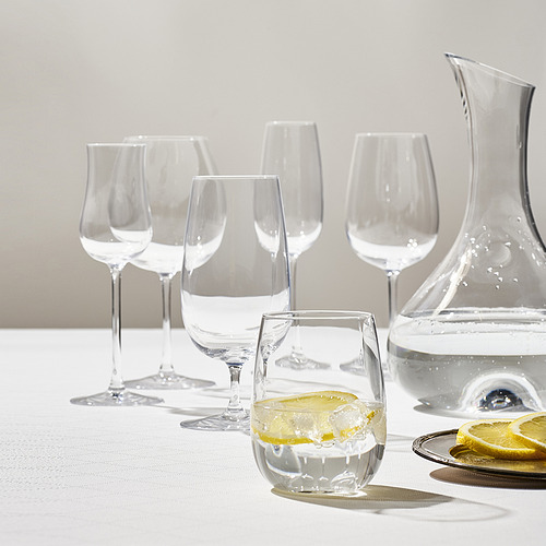 Seis vasos de cristal STORSINT y jarra sobre mantel blanco con rodajas de limón.